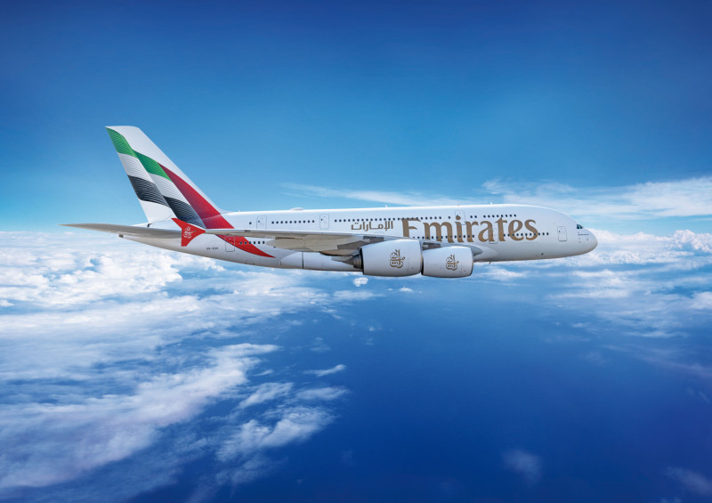 Emirates Airbus A380 flying in a clear blue sky above the clouds, featuring the airline's branding and UAE flag on the tail.
