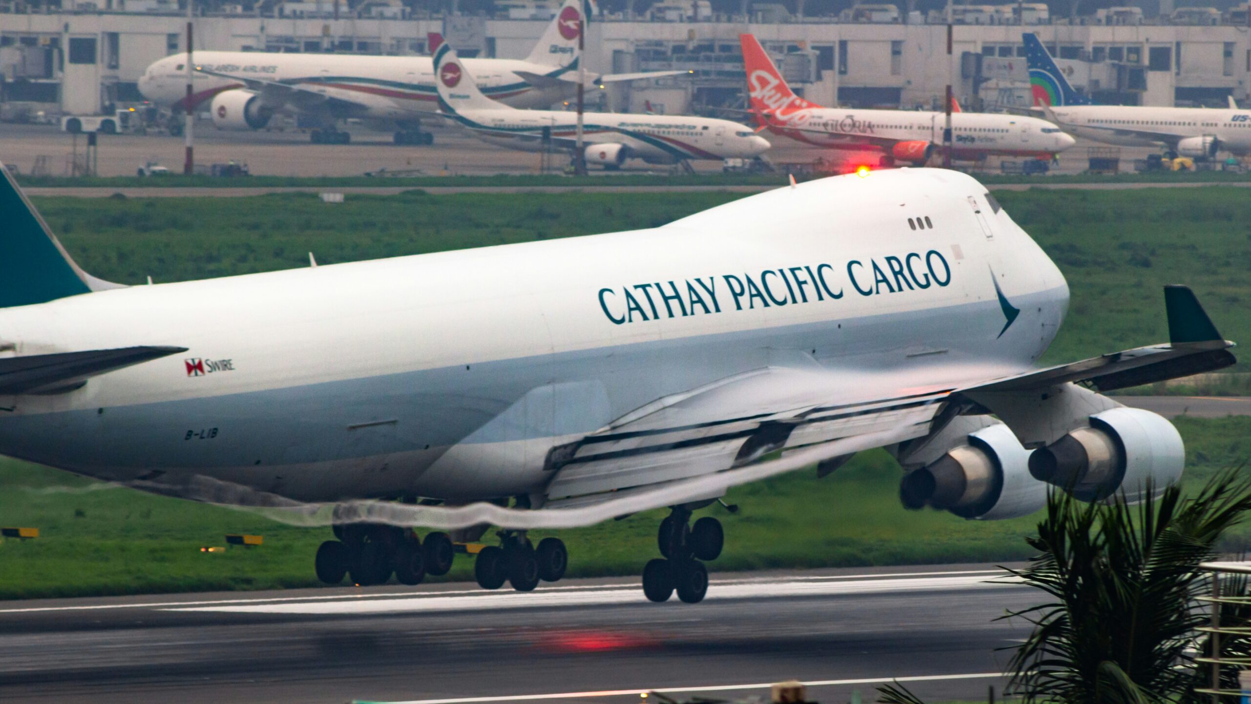 A Cathay Pacific Cargo aeroplane descending for landing, with its landing gear deployed against a backdrop of cloudy skies.
