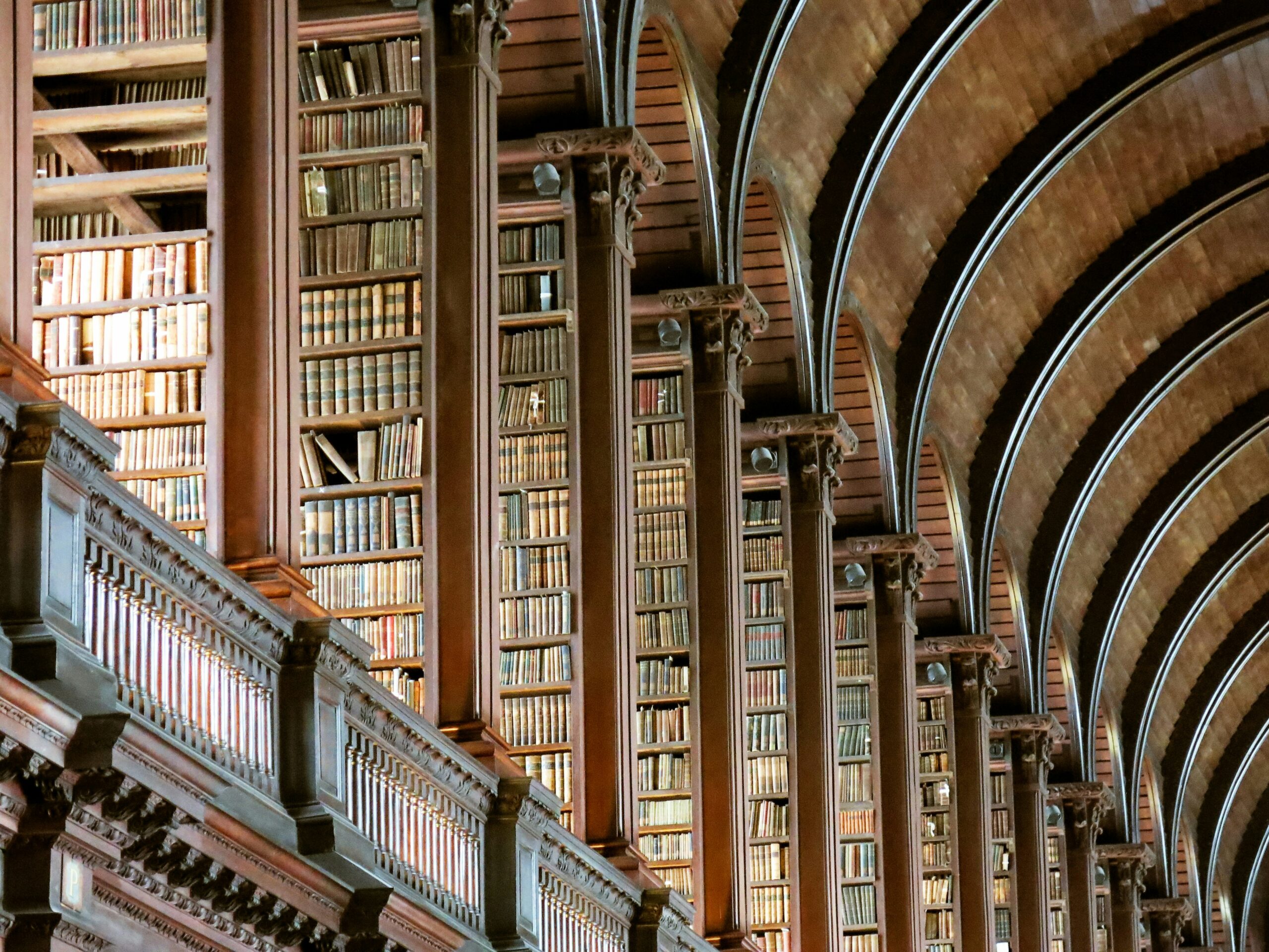 The Long Room Of The Old Library At Trinity College, Dublin, Ireland. Rows of tall wooden bookshelves filled with old books inside a historic library with arched ceilings.