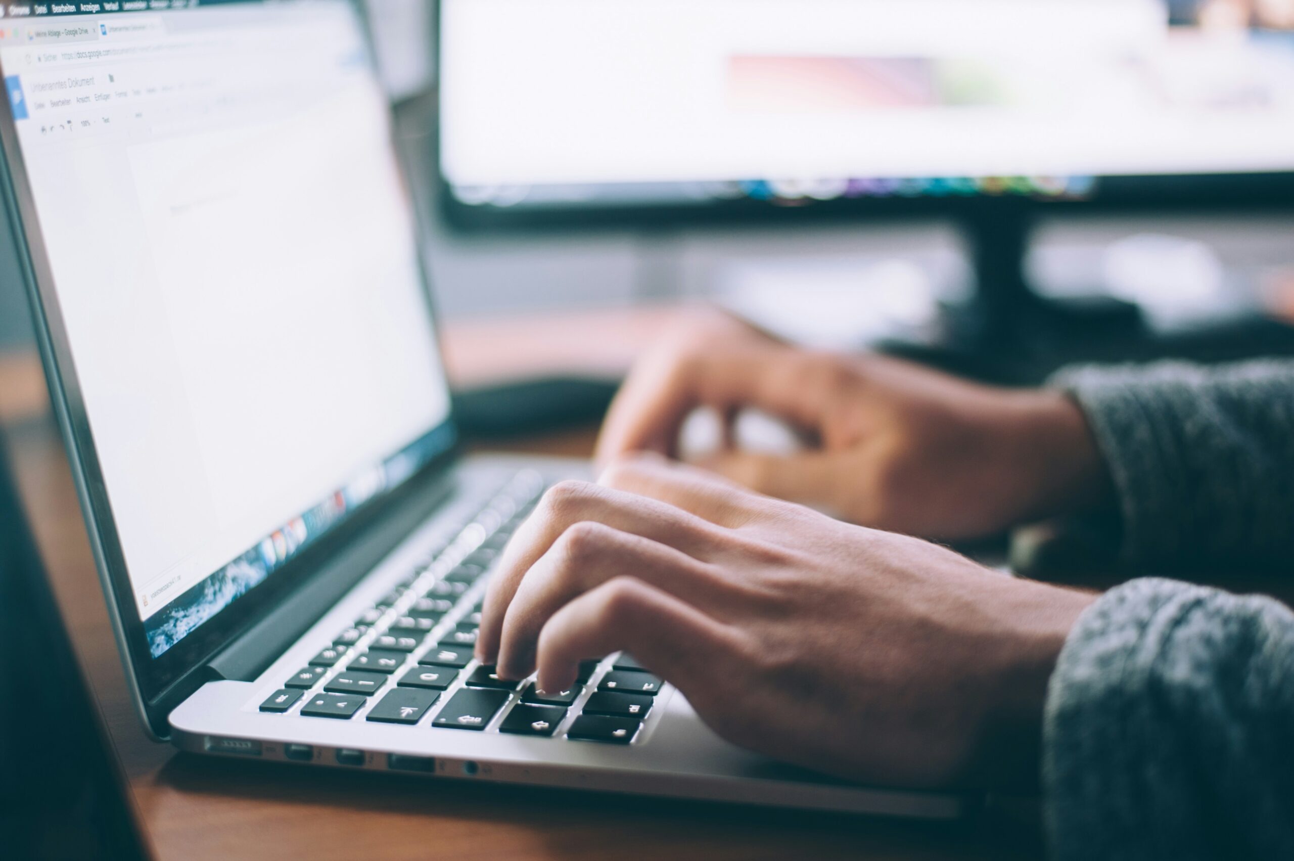 A close-up of a person’s hands typing on a laptop, showcasing the keyboard and screen.