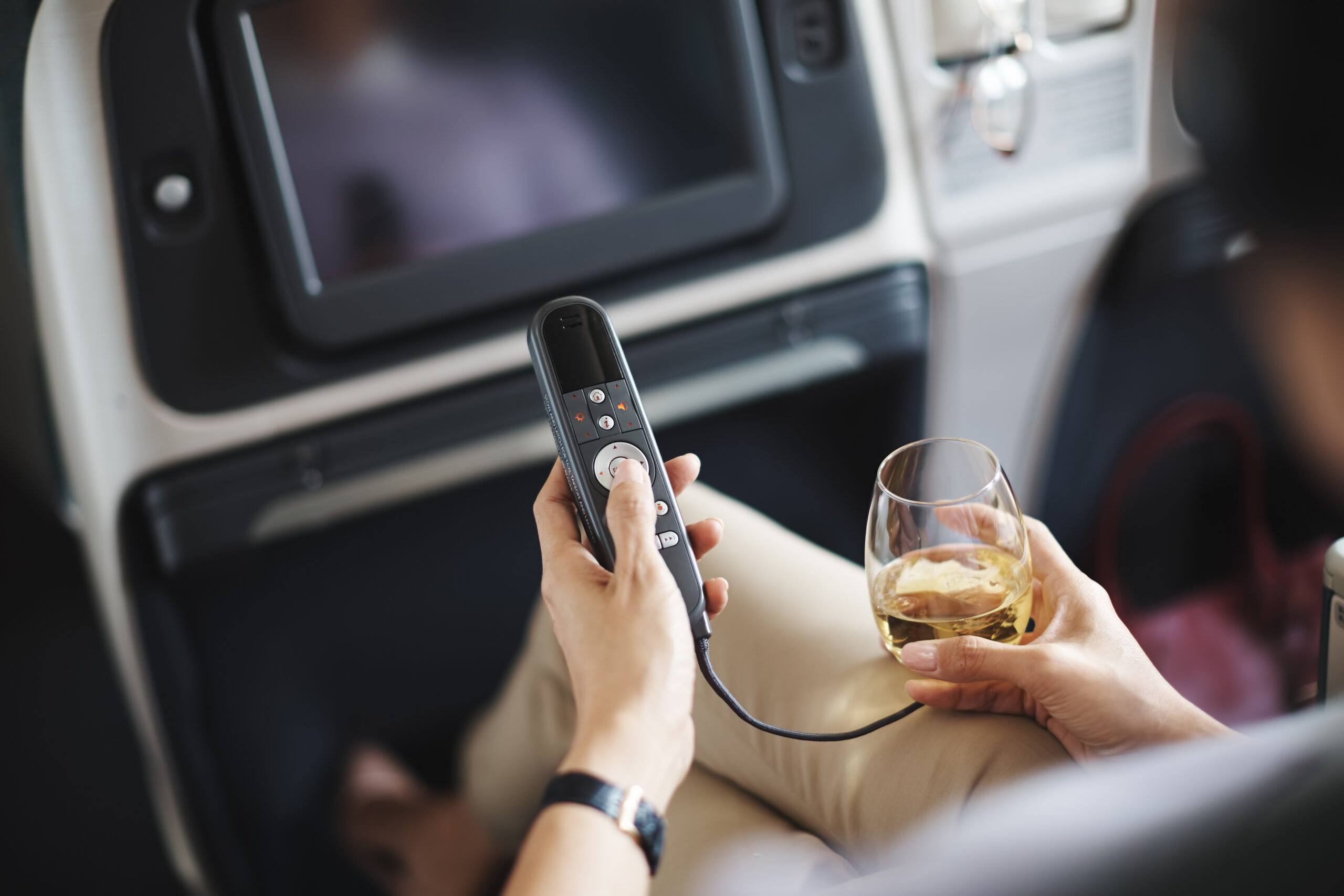A traveller holding a glass of white wine while using the in-flight entertainment remote control on a Cathay Pacific flight.