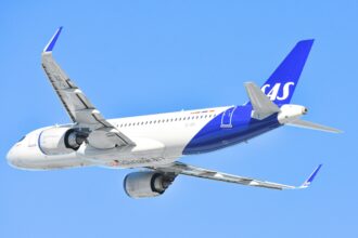 A Scandinavian Airlines (SAS) Airbus aircraft with a blue and white livery is soaring through a clear blue sky.