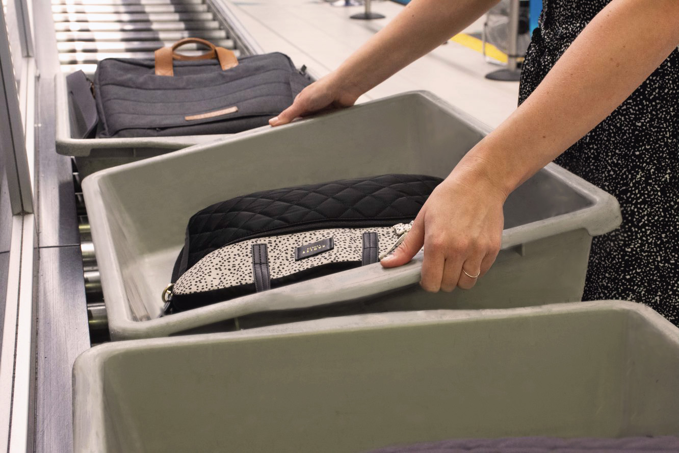 A person packs their bag into an airport security tray.