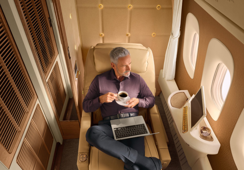 A man sits in First Class onboard an Emirates flight, enjoying a coffee.