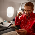 A passenger smiles as he orders on his phone onboard an aircraft.