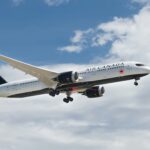 Air Canada airplane in mid-air with landing gear extended, flying through partly cloudy skies.