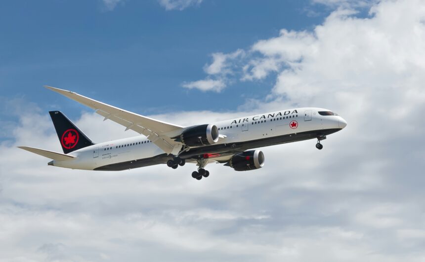 Air Canada airplane in mid-air with landing gear extended, flying through partly cloudy skies.