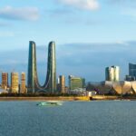 Waterfront view of Hangzhou skyline, showcasing modern architecture with futuristic skyscrapers and the distinctive Lotus-Flower-Shaped building under a clear blue sky, reflecting in the river.