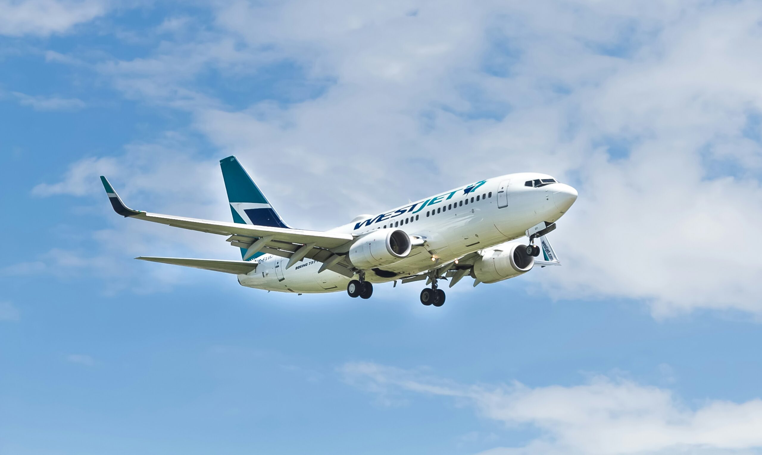 A WestJet Boeing 737 airplane flying against a blue sky with scattered clouds, preparing for landing