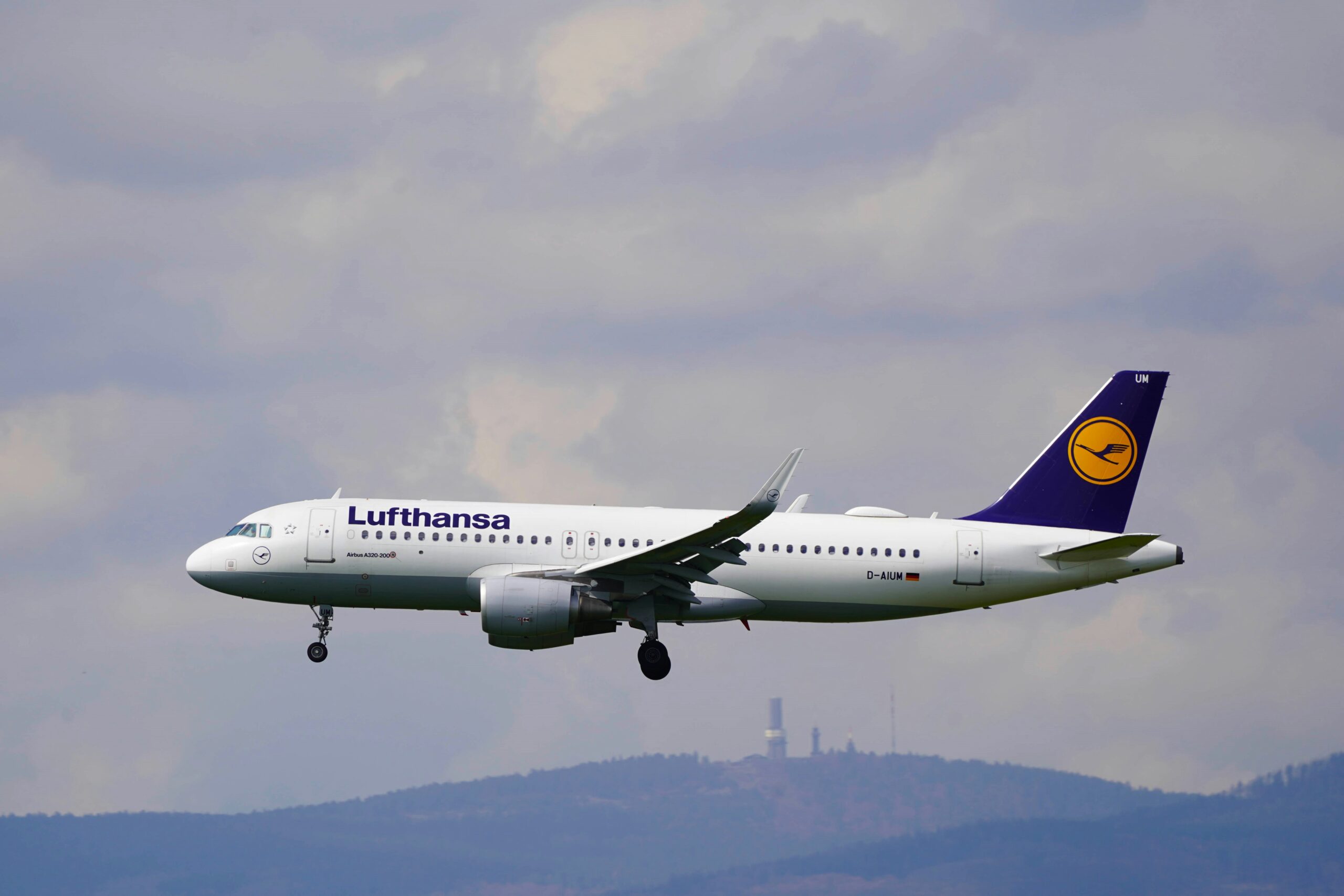 Lufthansa Airbus A320 flying through cloudy skies with landing gear extended.