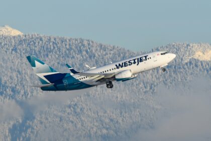 A WestJet airplane climbing through the sky, with snowy mountains in the background, showcasing a clear blue atmosphere.