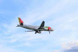 Aeroplane with colourful tail and engines, flying against a backdrop of a bright blue sky with scattered clouds. The scene feels calm and serene.