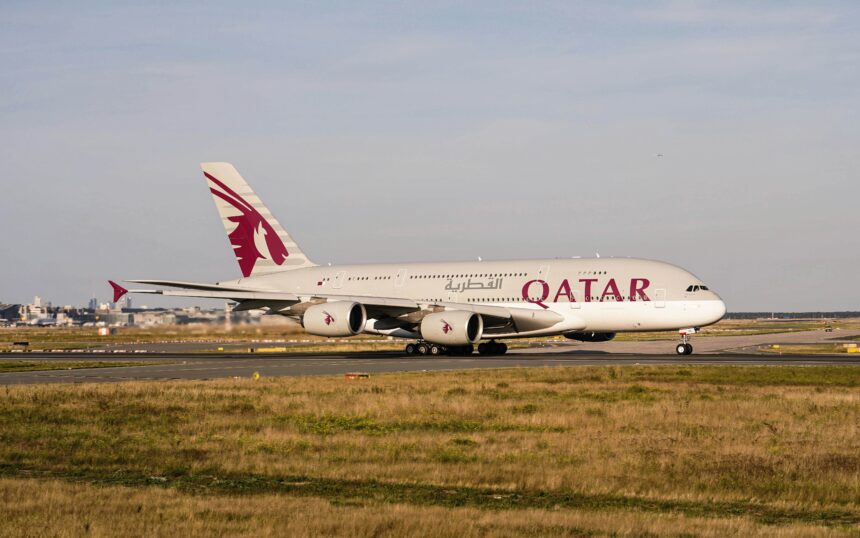A Qatar Airways plane soars above golden clouds during sunset, casting a serene glow.