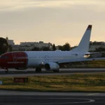 A photo of a Norwegian plane on a Runway at Sunset