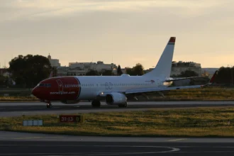 A photo of a Norwegian plane on a Runway at Sunset