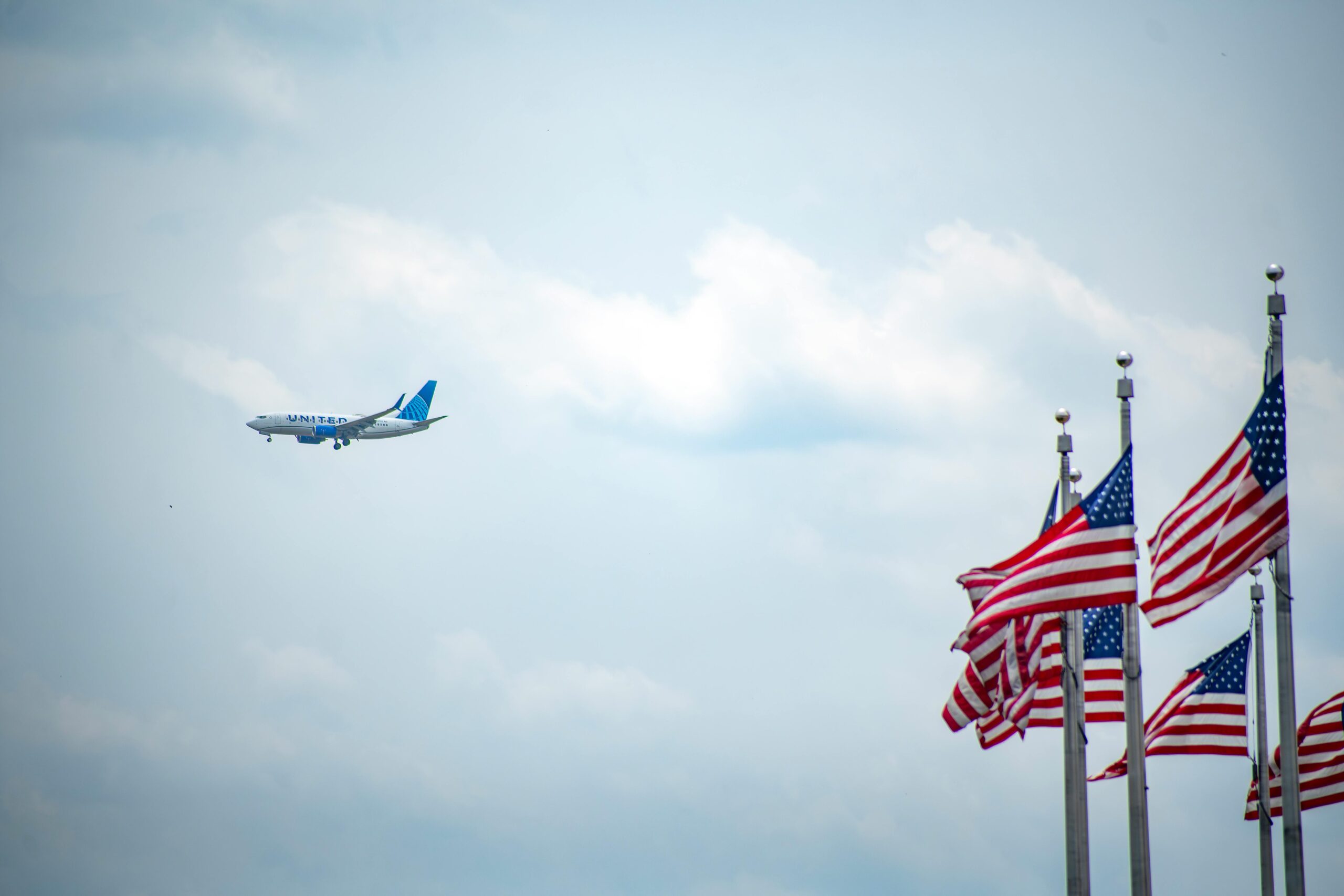 An image of a United Airlines aircraft flying in the distance with American flags in the foreground.