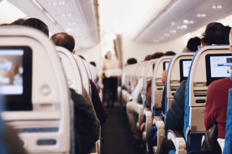 Picture of a full plane taken from the inside showing the entertainment screens and lots of passengers in their seats
