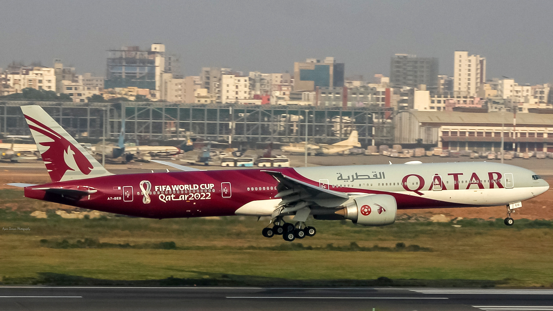 A Boeing 777 from Qatar Airways landing at an airport. The plane has a special red and white livery to commemorate the 2022 FIFA World Cup.