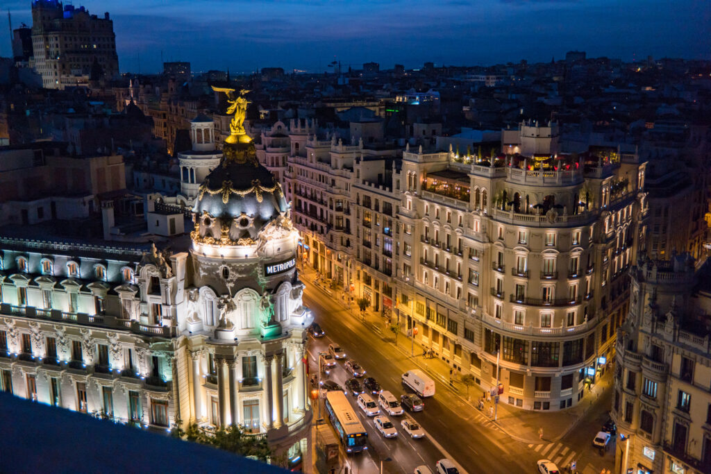 A nighttime view of the Gran Vía, Madrid, with the famous Metropolis building in front.