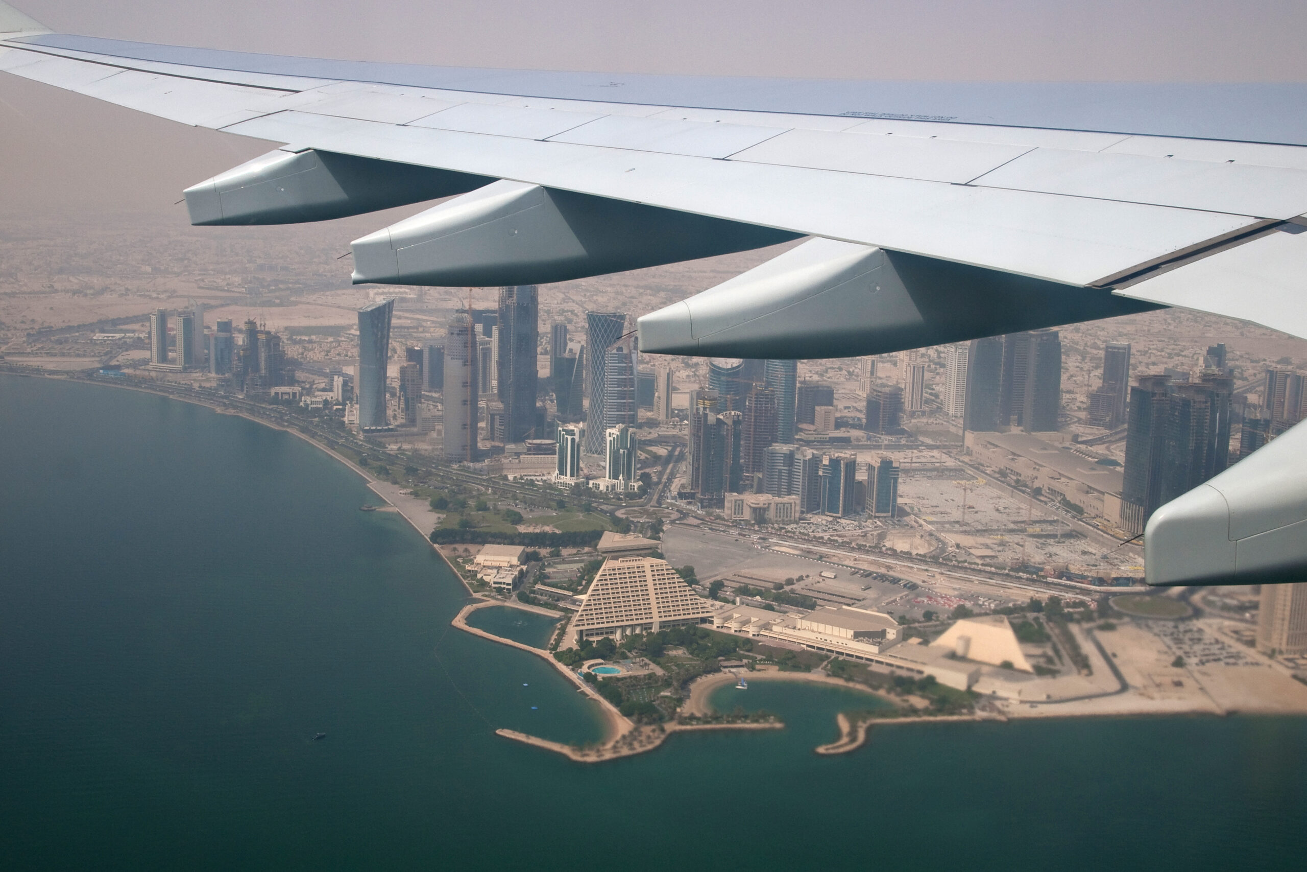 A coastal view of Doha's skyline from a plane window.