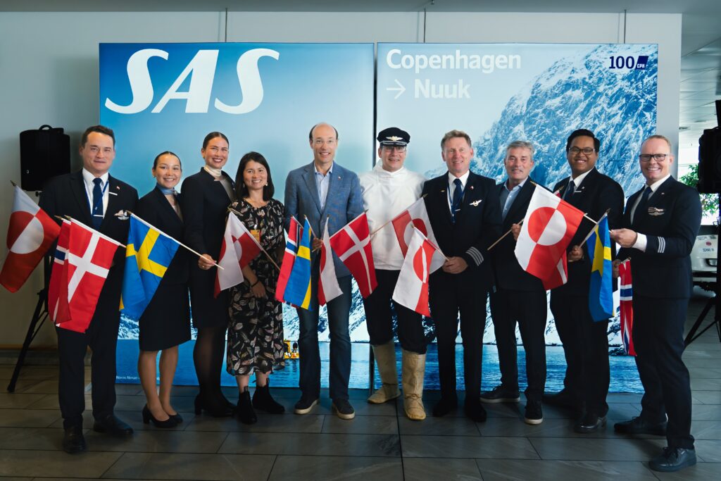 People standing and smiling in a line holding flags representing Denmark, Sweden and Greenland.