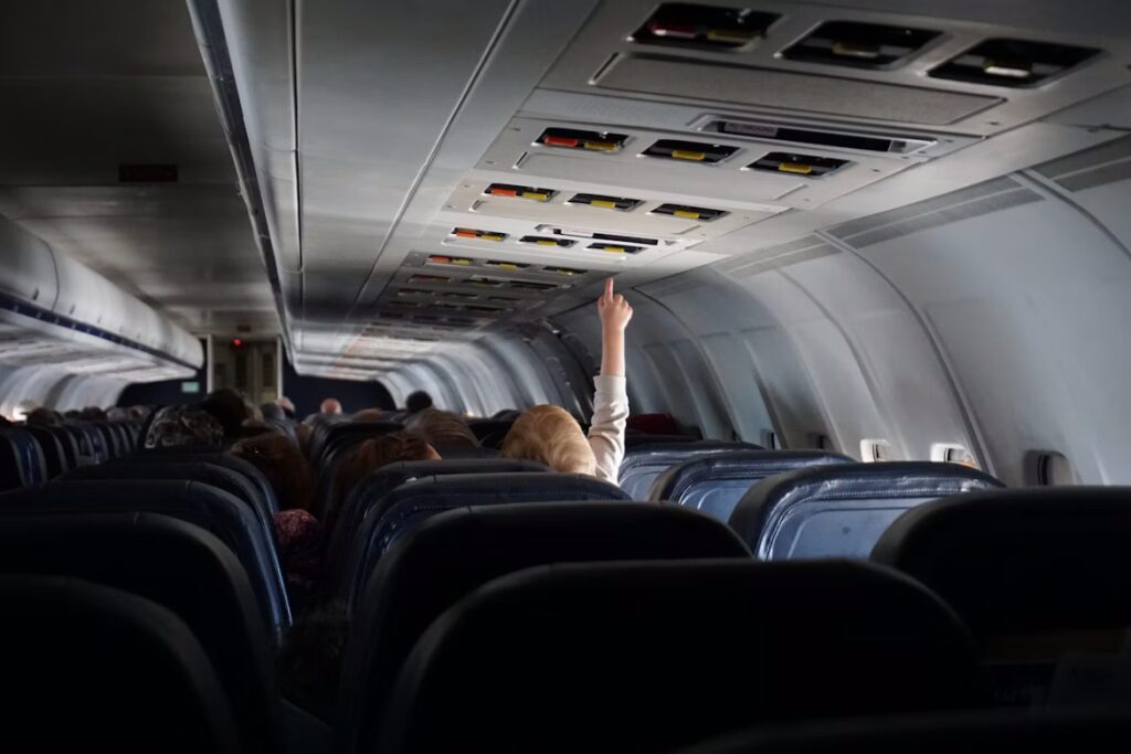 Passenger on an aircraft reaching for ceiling panels above the seats. 