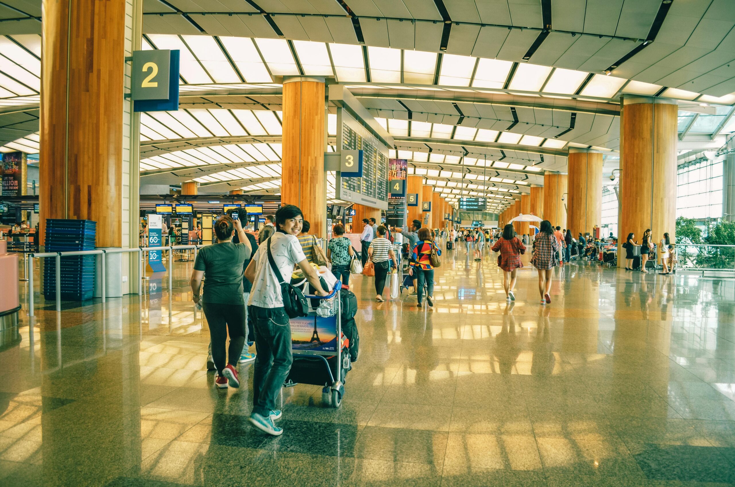 A boy standing smiling at the airport terminal with people in the background.
