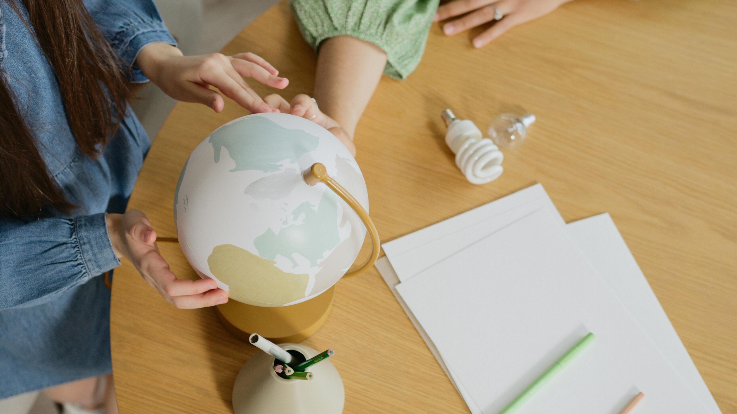 People holding a globe with art supplies on a desk