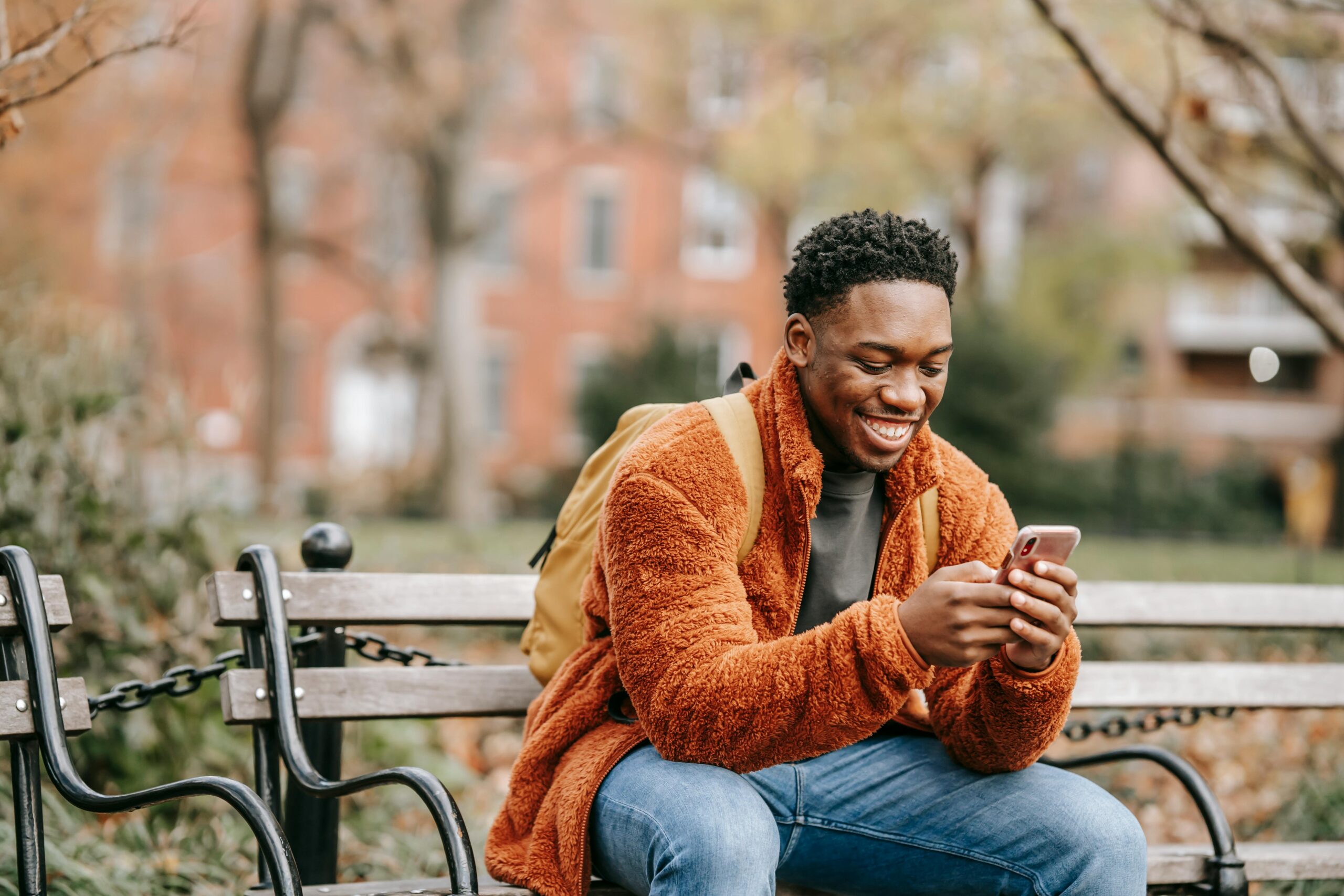 A smiling man sitting on a bench in town using his phone