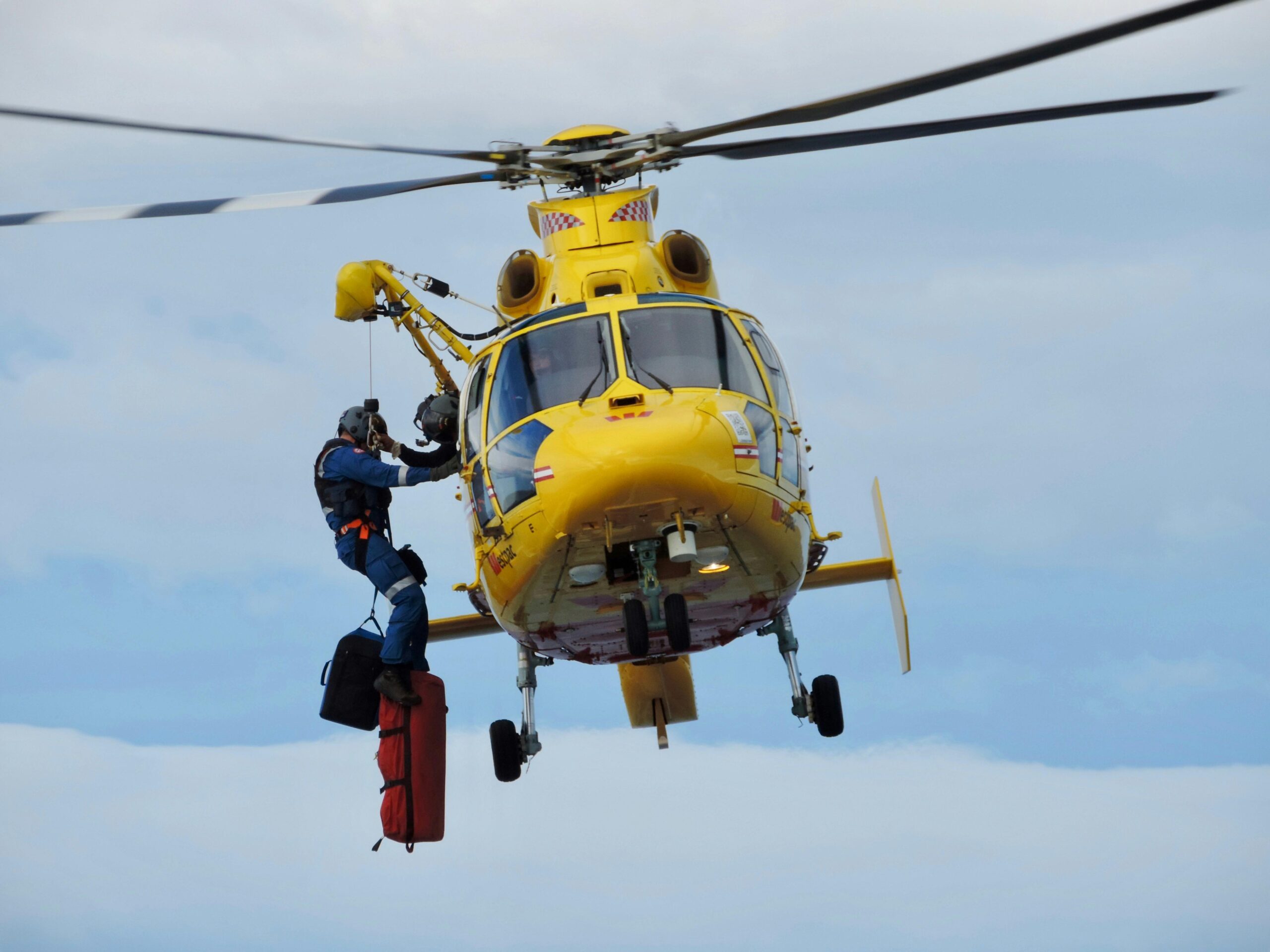 Yellow Helicopter in the air with a person hanging from it