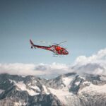 Red helicopter flying above the mountains and white clouds on a blue sky