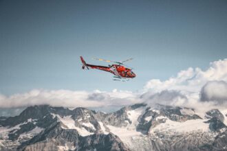 Red helicopter flying above the mountains and white clouds on a blue sky