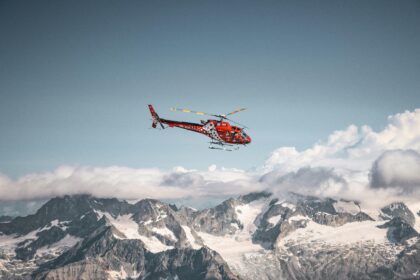 Red helicopter flying above the mountains and white clouds on a blue sky