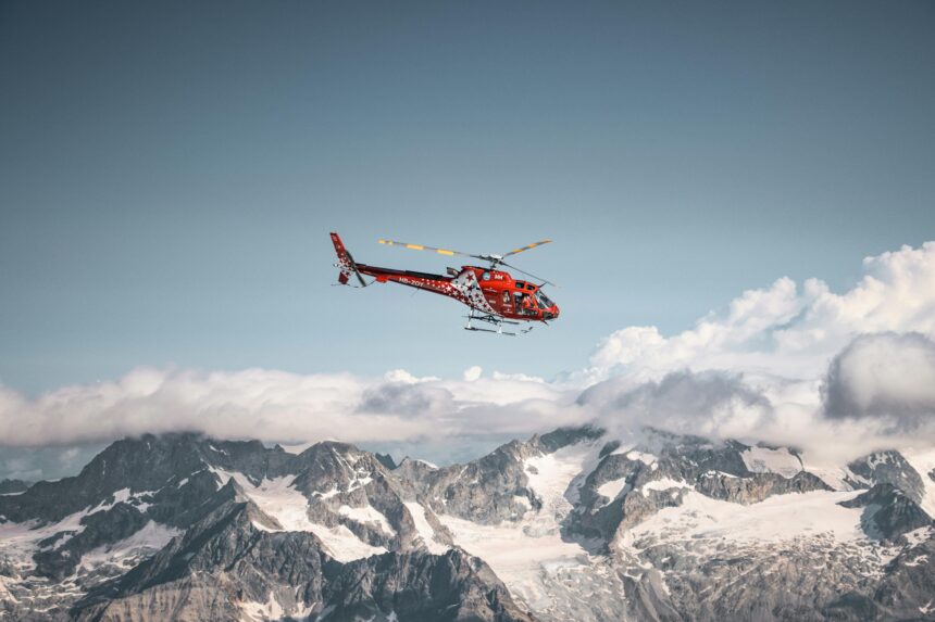 Red helicopter flying above the mountains and white clouds on a blue sky