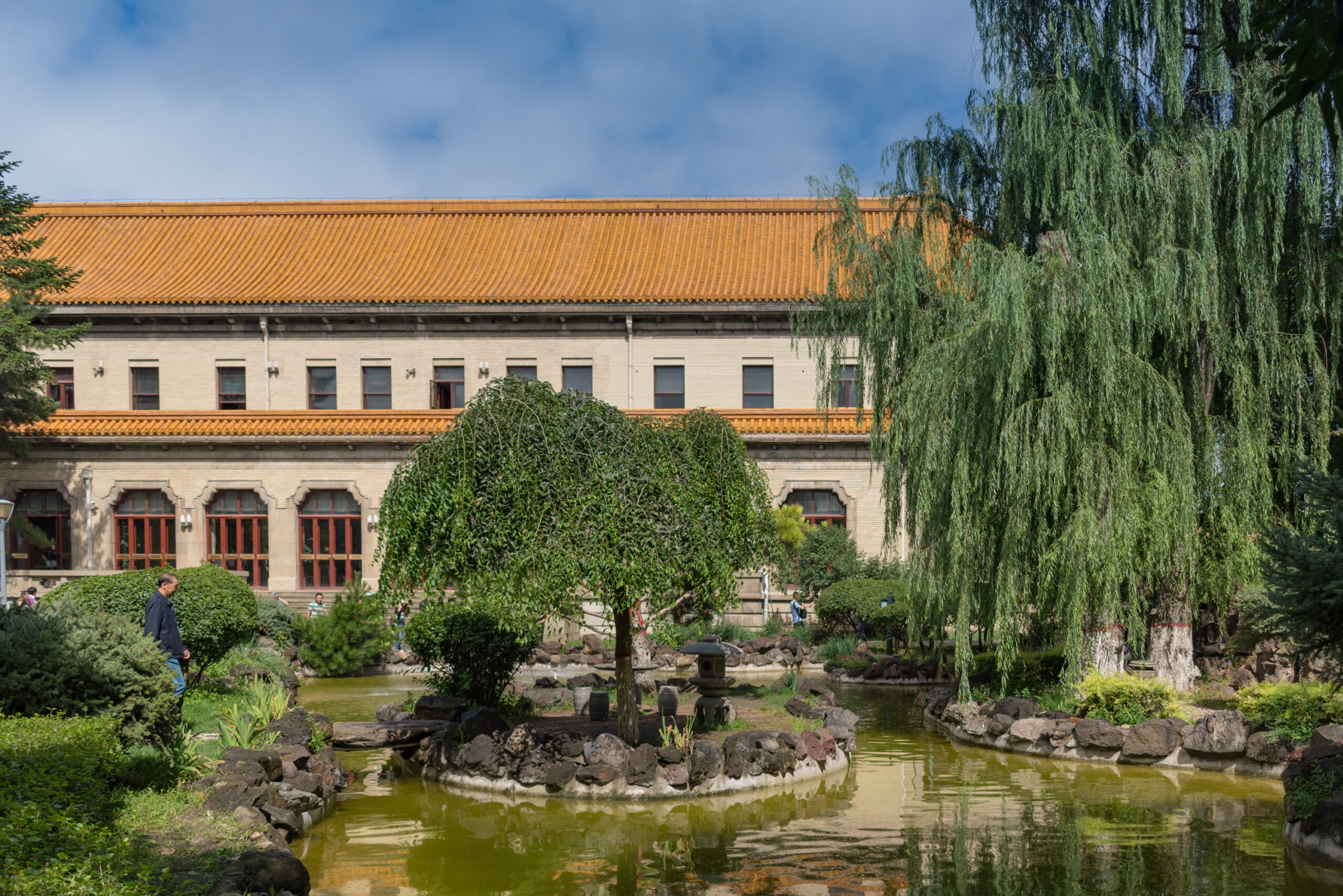 The Museum of the Imperial Palace of Manchukuo, a Japanese-built Chinese palace for the country's last emperor. There are willow trees on the banks of a pond in front of the palace.