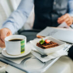 A well-dressed man in a suit enjoys a cup of coffee and a dessert offers by airBaltic inflight service.