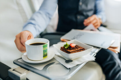 A well-dressed man in a suit enjoys a cup of coffee and a dessert offers by airBaltic inflight service.