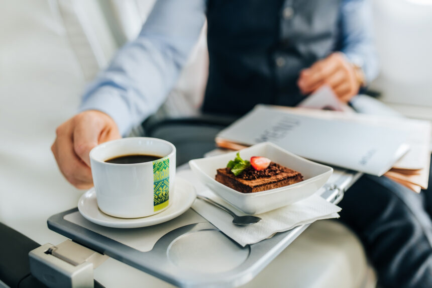A well-dressed man in a suit enjoys a cup of coffee and a dessert offers by airBaltic inflight service.
