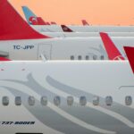 Turkish Airlines' aeroplanes are parked on the tarmac under a clear blue sky.
