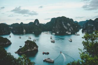 A stunning view of the serene Ha Long Bay, Vietnam, featuring green limestone islands and several boats cruising on the calm waters.