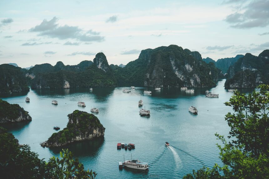 A stunning view of the serene Ha Long Bay, Vietnam, featuring green limestone islands and several boats cruising on the calm waters.