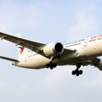A Boeing Dreamliner aircraft in mid-air with landing gear deployed.