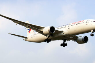 A Boeing Dreamliner aircraft in mid-air with landing gear deployed.