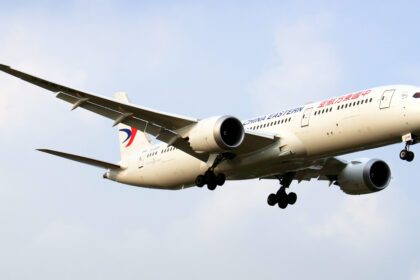 A Boeing Dreamliner aircraft in mid-air with landing gear deployed.