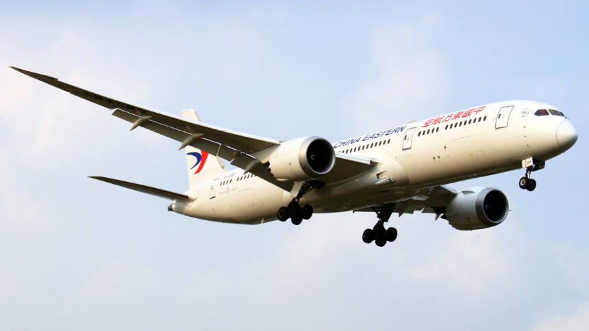 A Boeing Dreamliner aircraft in mid-air with landing gear deployed.