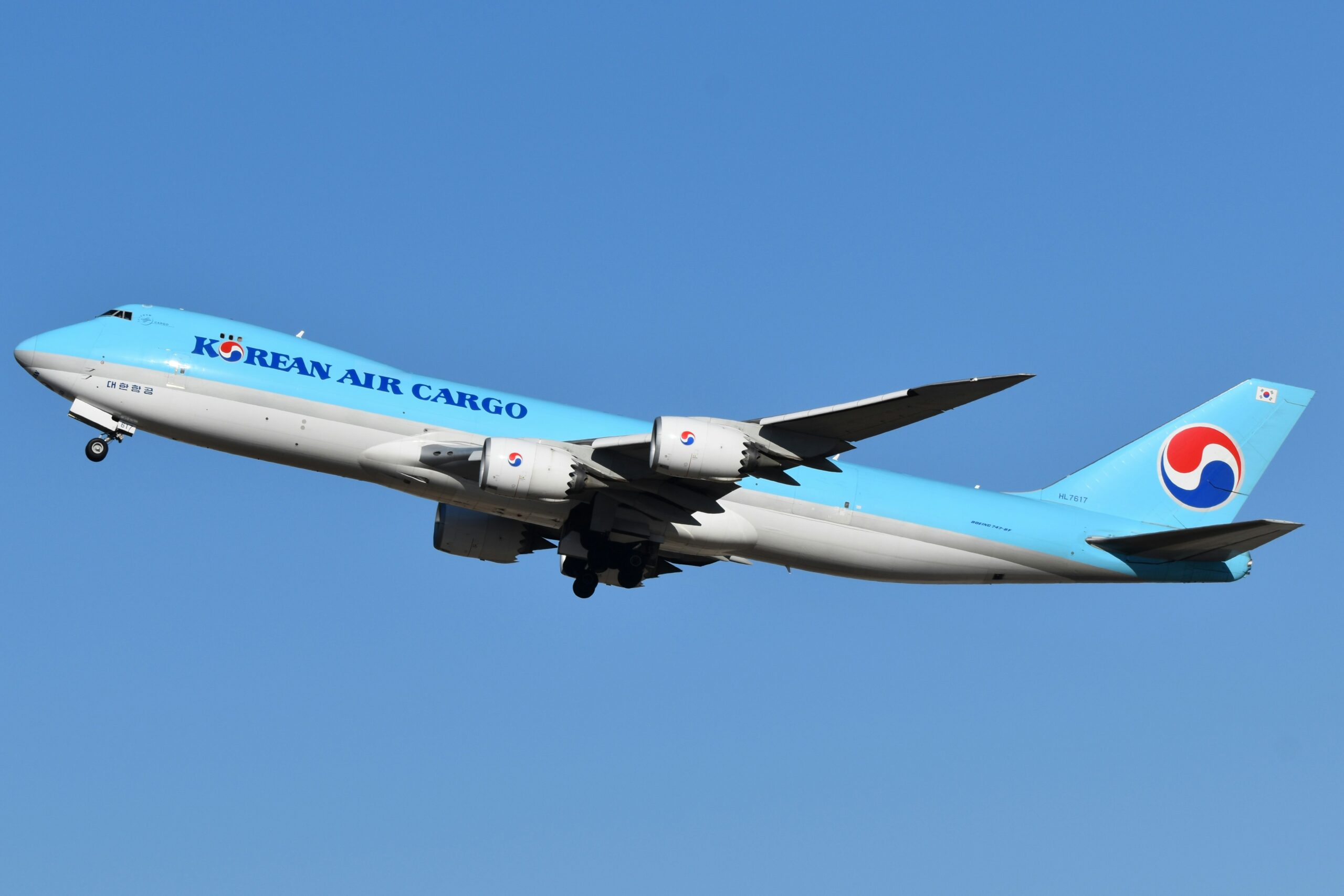 Blue Korean Air Cargo plane takes off against a clear blue sky, showcasing its powerful engines and sleek design, evoking a sense of movement and scale.