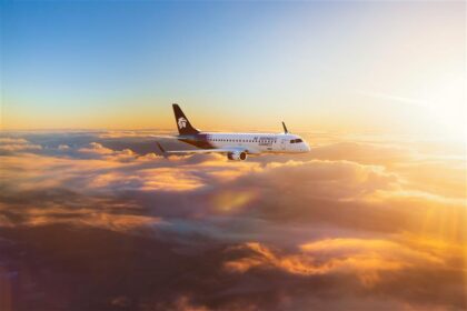 An Aeromexico Connect Embraer E190 aircraft flying above the clouds during sunset, with golden light illuminating the sky and cloudscape.