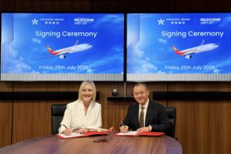 The representatives were attending the signing ceremony. Two individuals signing documents at a table, with a large screen displaying information displaying the aeroplane with the logo of Hong Kong Airlines in the background.