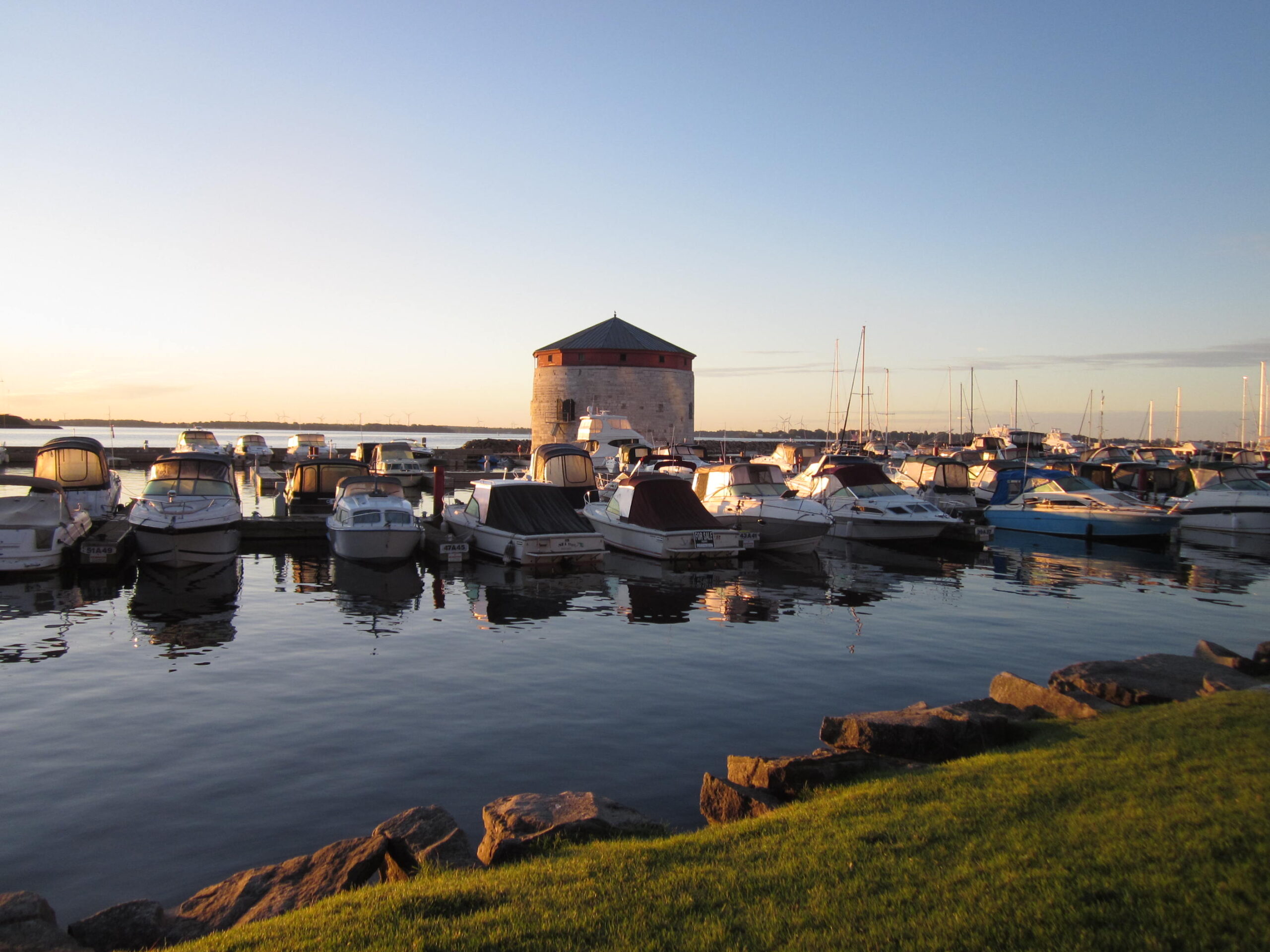 A picture of the waterfront in Kingston, Ontario, with many boats moored up in front of a round tower with a conical roof.