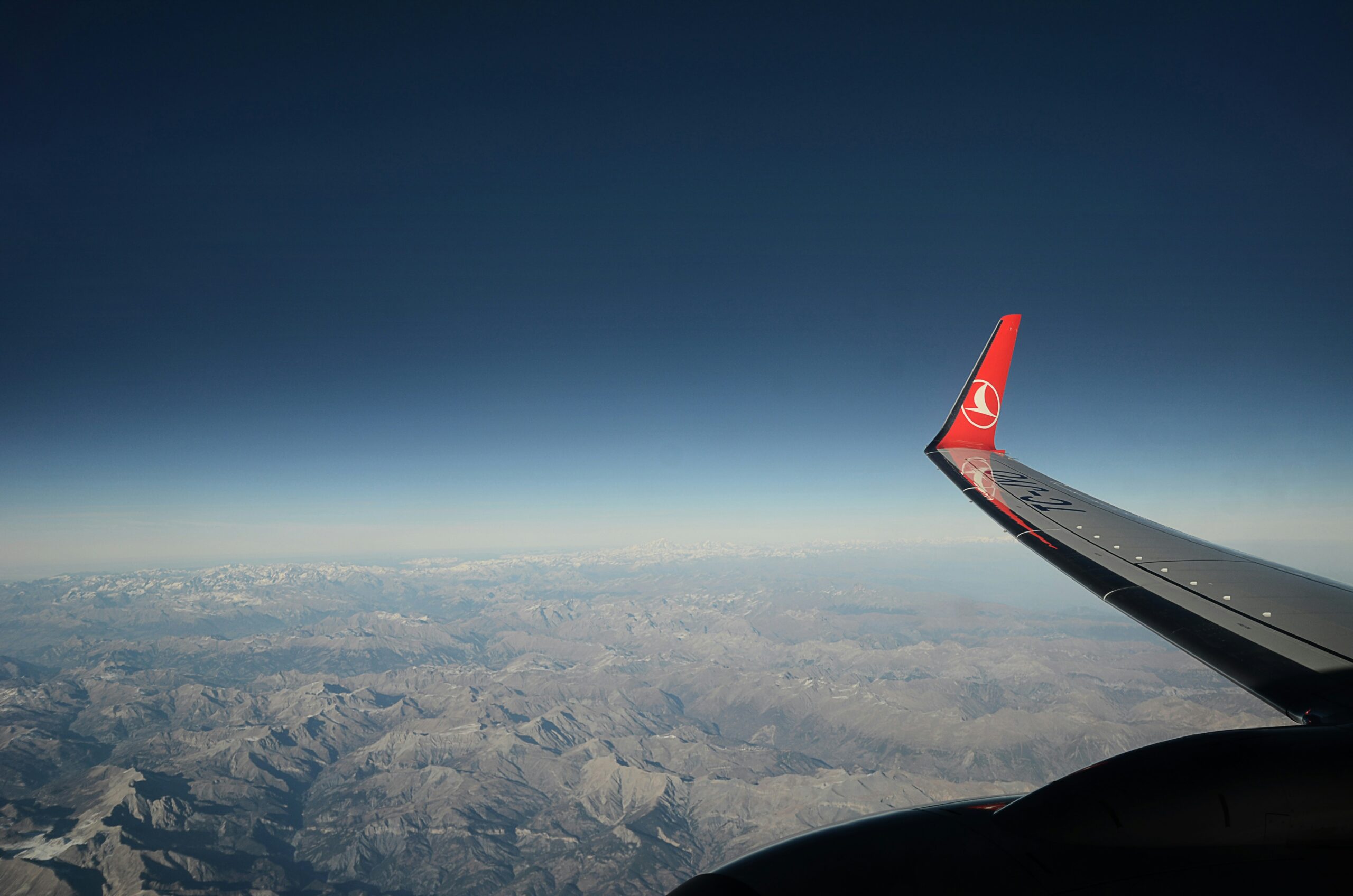 A Turkish Airlines aeroplane wing viewed from the side, with sunlight reflecting off its surface against a backdrop of clouds.